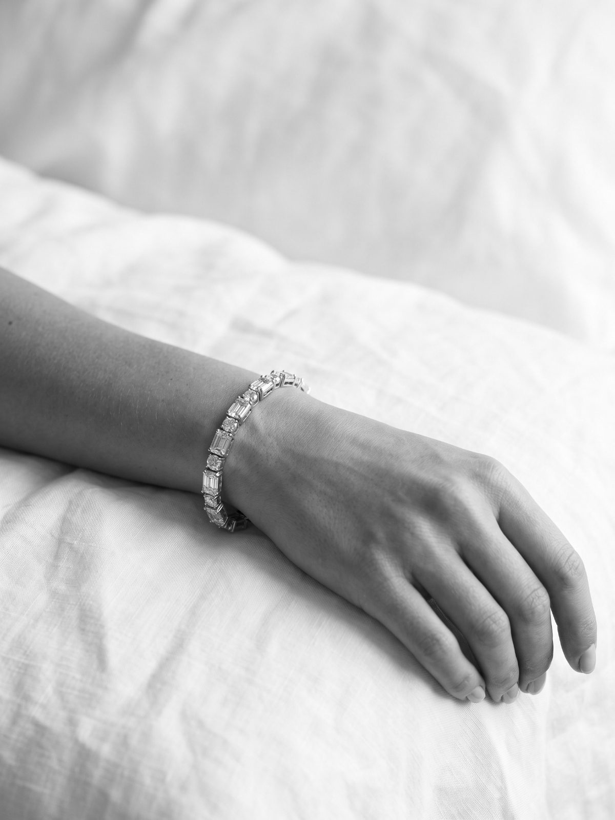 Diamond tennis bracelet on a relaxed wrist against linen