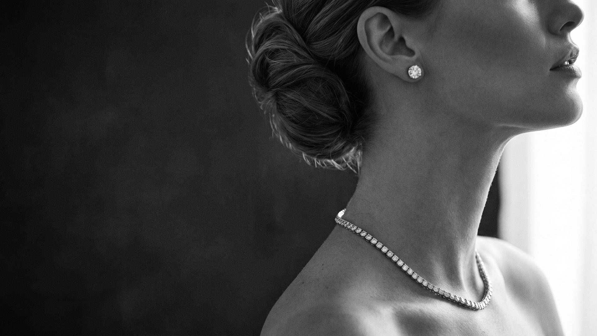 Woman in profile wearing a diamond tennis necklace and round diamond stud earrings