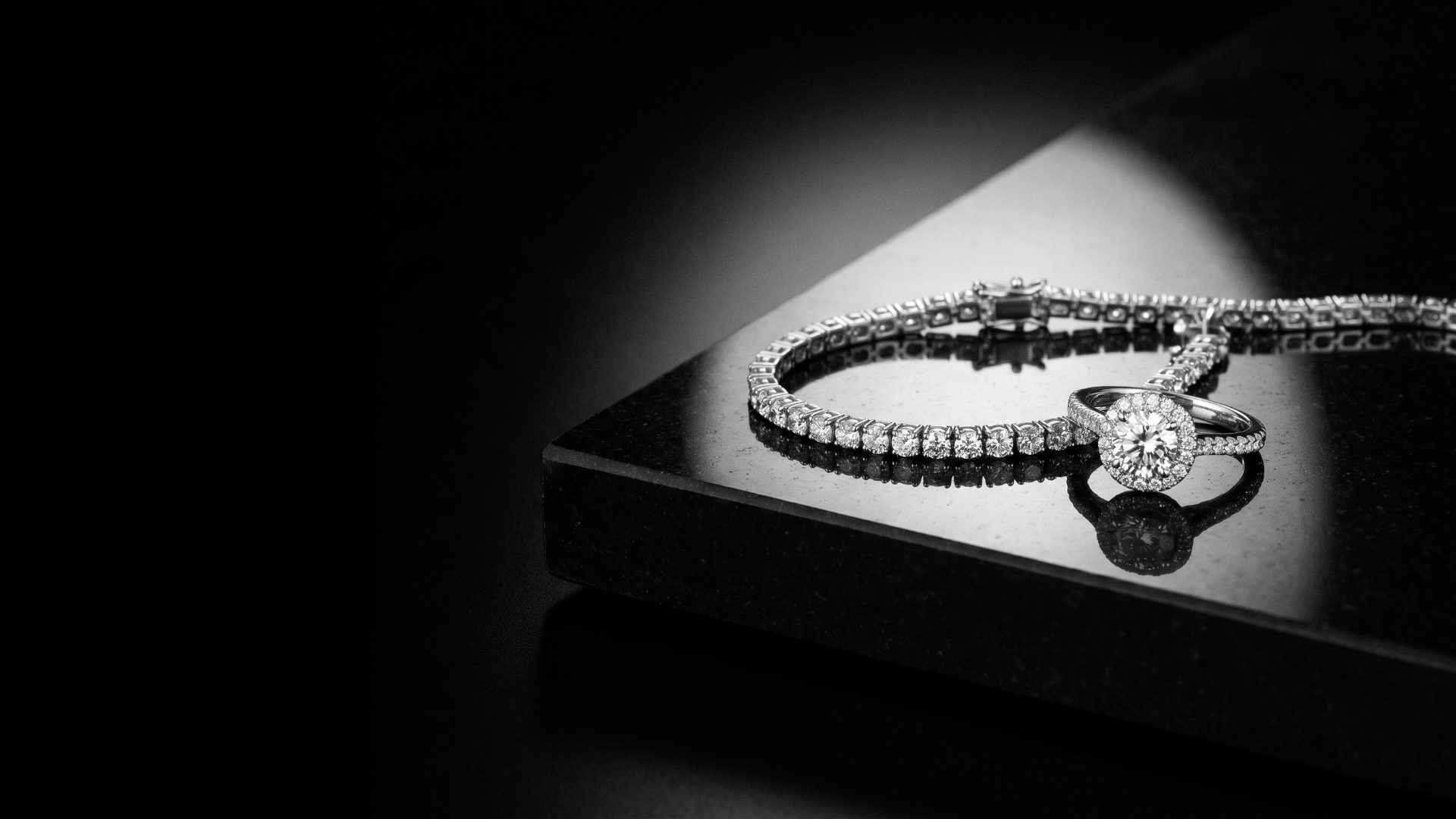 Diamond tennis bracelet and halo engagement ring on polished black stone